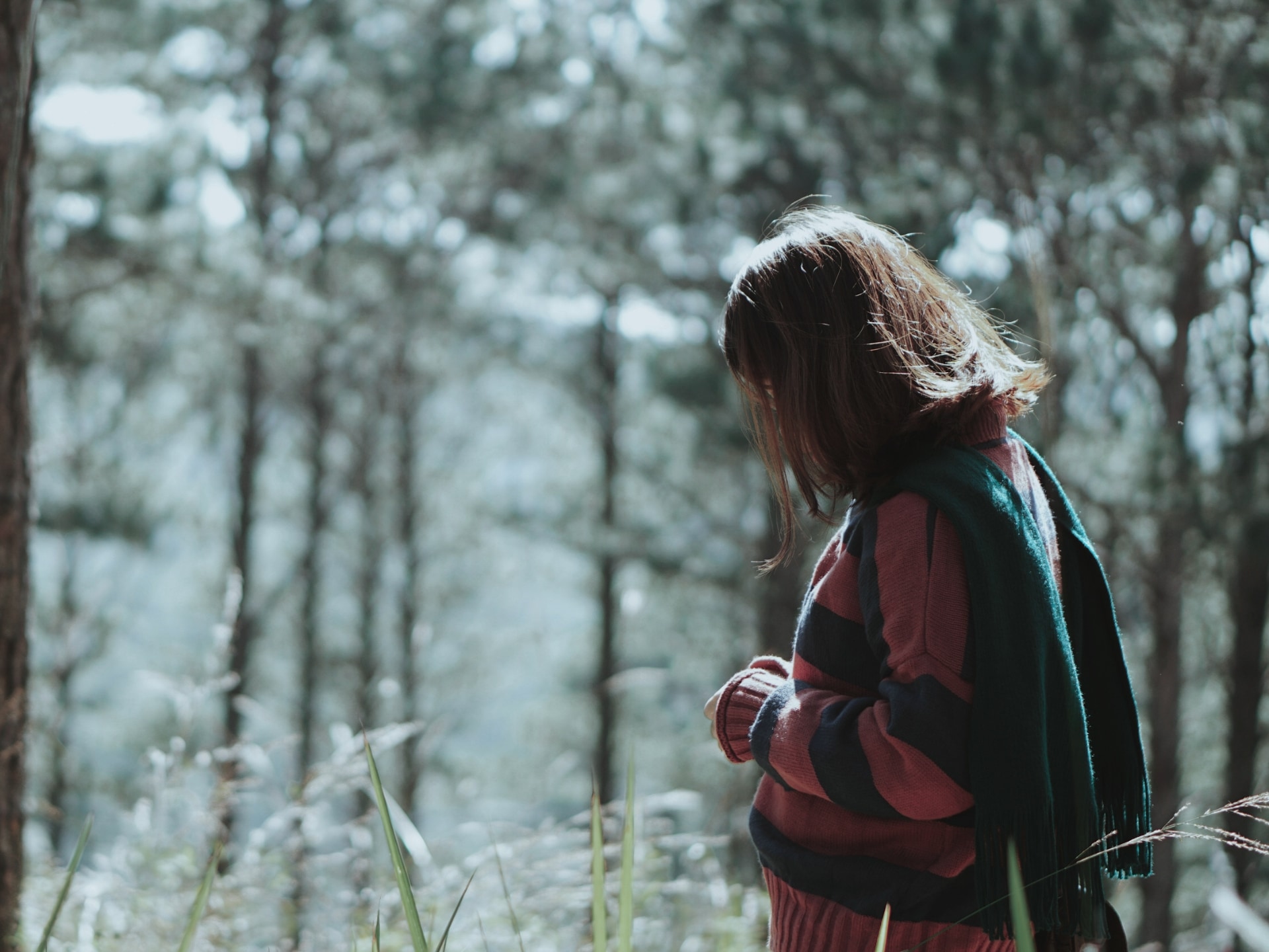 Person standing in a field of tall grass, facing right and looking down at the ground
