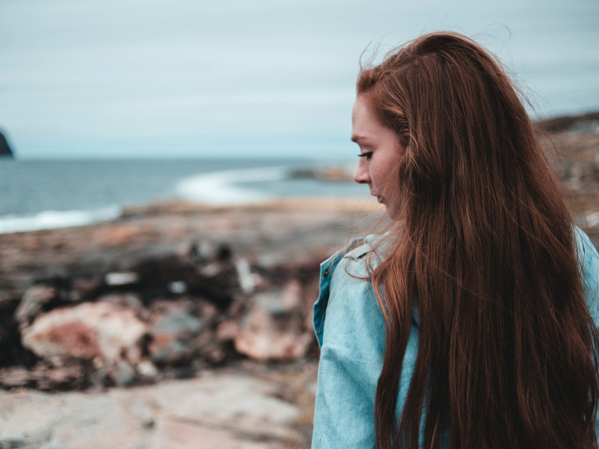 Young red haired woman at the beach by herself, looking down to her left