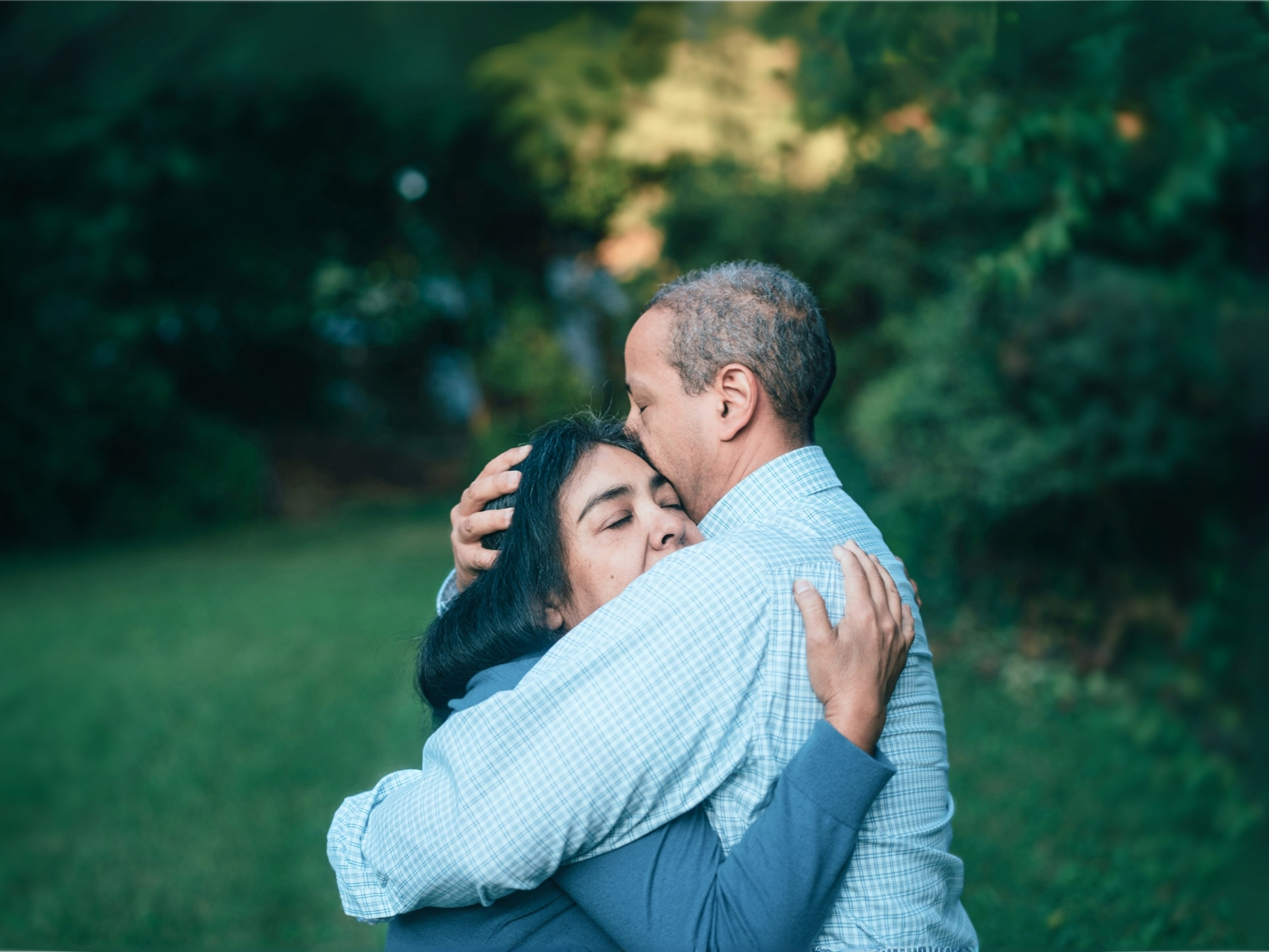 Man and woman embracing outdoors, with the man kissing the woman’s forehead in a comforting gesture